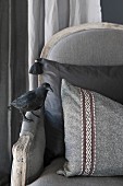 Antique grey armchair with scatter cushion and crow figurine on armrest