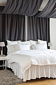 Bed with white bed linen and valance under canopy made from two lengths of black fabric