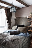 Fur rug and scatter cushions on comfortable bed in rustic bedroom with wood-clad walls and wood-beamed ceiling