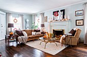 Sofa, armchair and brass and glass coffee table in front of festively decorated fireplace in American country-house living room