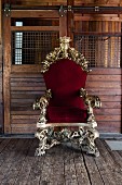 Opulent, ornate gilt throne with red velvet upholstery against board wall