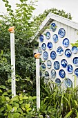 White gable-end wall of wooden cabin decorated with blue plates and ornamental wooden posts in garden