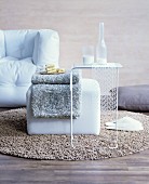 Woollen blanket on pouffe and delicate side table on woollen rug