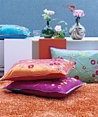 Decorative, colourful, floral scatter cushions on orange woollen rug in front of retro vases and flowers on sideboard