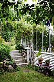Neben teilweise sichtbarem Gewächshaus mit weissen Holz- und Glaselementen Treppe aus Beton in sommerlichem Garten