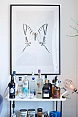 Drinks trolley below framed picture of butterfly