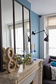 Mirror, wooden ornament and glass candle lantern on mantelpiece in Scandinavian interior
