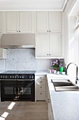 Kitchen counter with pale marble worksurface and integrated sink; fitted cupboards with extractor hood above black cooker in background