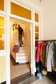 Coat rack next to lattice door in hallway and man walking up white wooden staircase in rustic stairwell
