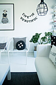 Patterned cushions on white metal chairs, motto made from decorative letters and framed photo on wall in corner of black and white room