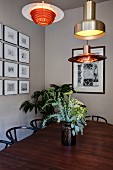 Various, retro-style pendant lamps above vase of flowers on dining table and classic chairs; framed pictures on wall