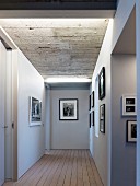 Illuminated hallway with gallery of black and white photos below exposed concrete ceiling