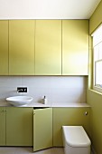 Green fitted cupboards and white countertop basin in bathroom