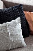 Cushions with pale fur cover, black structured cover and copper satin cover in corner of sofa