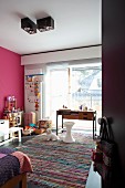 Blick in Mädchenzimmer mit buntem Flickenteppich, weißem Hocker und filigranem Schreibtisch