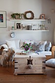 Comfortable wicker sofa below elegant floating shelves and vase of mallows on rustic trunk table