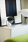 Weißes Sideboard mit gerahmtem Bild, Zimmerpflanze und Designertischleuchte