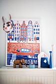 Framed poster, rabbit mask, elephant ornament and candlesticks on white wooden surface
