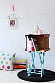 Small cabinet made from old wooden crate on top of light blue folding stool
