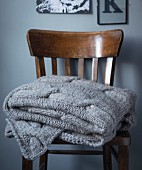 A grey blanket with a cable knit pattern on a wooden chair