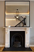 Mirror on white mantelpiece reflecting staircase and designer lamp in renovated interior