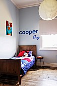 Colorful patchwork blanket on wooden bed in light blue room corner, on wall 'Superman' picture and decorative letters