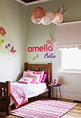 Pink pillows on wooden bed in girl's room, decorative letters on wall, and wall decals with floral motifs