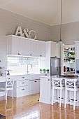 Counter and bar stool in an open fitted kitchen with white, country-style fronts with shiny floorboards