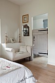 White couch against protruding section of wall and rustic door leading to ensuite bathroom
