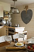 Breakfast ingredients on table in rustic fitted kitchen with large heart-shaped decoration on wall