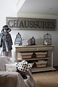 Armchair covered in throw, antique-style console table, tailors' dummy wearing hat and coat and vintage sign on wall