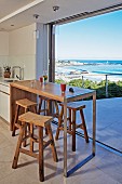 Modern wooden counter and rustic bar stools in front of open terrace doors with panoramic sea view