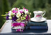 Romantic flower arrangement with pink ribbon next to antiquarian books and vintage-style teacup on vintage case