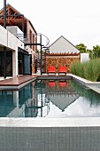 Modernes Wohnhaus mit Pool, Stahlwendeltreppe und orangefarbenen Ligepolstern vor Natursteinwand
