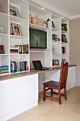 Study with laptop on desk below open-fronted white shelving with TV in contemporary interior