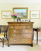 Antique chest of drawers with brass handles below framed pictures on wall painted yellow