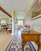 Pale, wooden antique console table in open-plan hallway with tiled floor and arched doorway