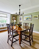 Antique dining table and chairs with carved backrests in green-painted dining room with sisal carpet