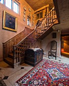 Orientteppich und antiker Truhe vor kunsthandwerklichem Holztreppenaufgang in einem Herrenhaus