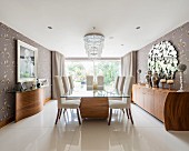 Glass-topped dining table on exotic-wood base and upholstered chairs in elegant dining room with glossy tiled floor