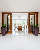 View from tiled foyer through open glass double doors flanked by planters into elegant dining area