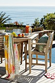 Sunny terrace with wooden table and chairs next to pool with sea view on background