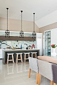 Dining set in front of counter and bar stools below row of pendant lamps with bird-cage lampshades