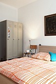 Old metal locker used as wardrobe and chair as bedside table next to double bed in bedroom