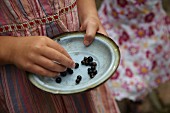 Vintage dish of blackcurrants held in girl's hands