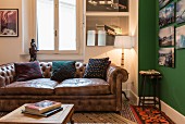 Scatter cushions on vintage leather sofa next to landscape photos on green wall