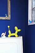 Yellow balloon-dog ornament in front of royal blue wall