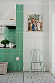 Pastellgrüner Stuhl vor weisser Holzverkleidung neben grün gefliestem Kochbereich in skandinavischer Küche