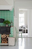 Gusseiserner Küchenofen mit Holzlager in grün gefliestem Kochbereich und offener Durchgang mit Blick ins Wohnzimmer