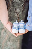 Couple holding tiny baby shoes in interlinked hands